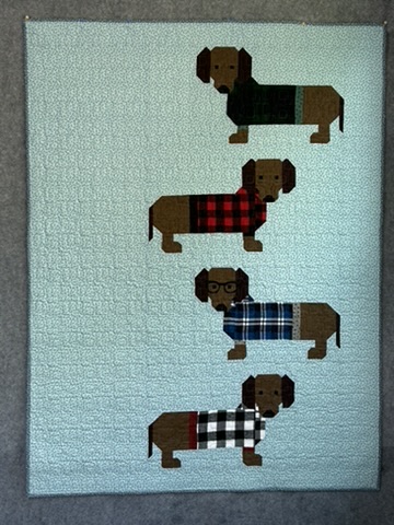 Weiner Dogs Baby Quilt by Michele Urbany Neely Puluti with four appliquéd dachshunds in patterned coats on a pale blue quilted background
