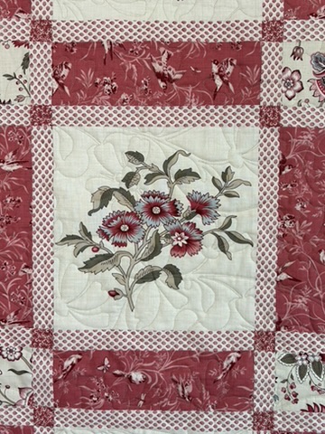 Close-up of The French General Quilt showing a red and cream floral panel, layered sashing, and curved quilting